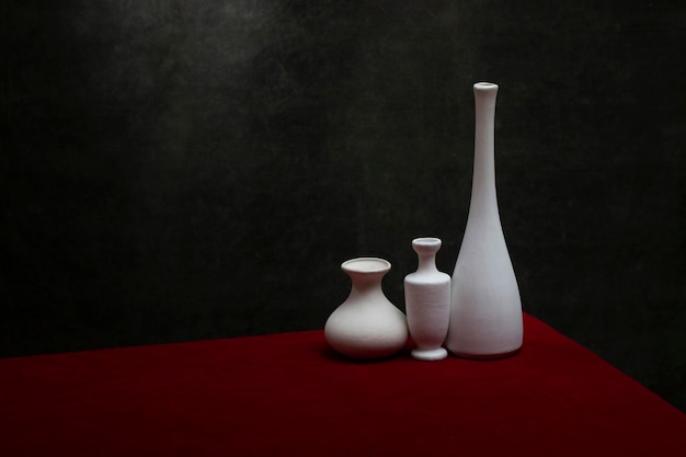 Nature morte aux vases blancs sur une table avec une nappe rouge