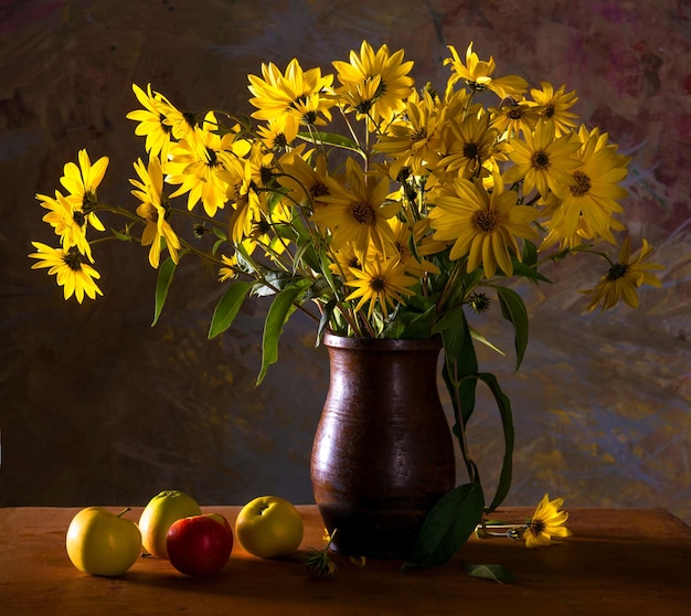 Nature morte avec bouquet de fleurs jaune vif (rudbeckia) dans un vase marron et des pommes