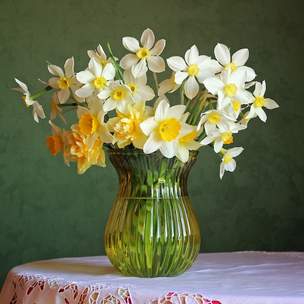 Nature morte avec un bouquet de jonquilles dans un vase en verre sur une table avec une nappe blanche avec de la dentelle