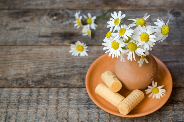 Nature morte d'un bouquet de pâquerettes dans un vase et des tubes de gaufres. Style rustique en bois.