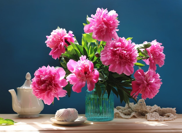 Nature morte avec un bouquet de pivoines roses et de guimauves. Fleurs du jardin dans un vase en verre bleu.