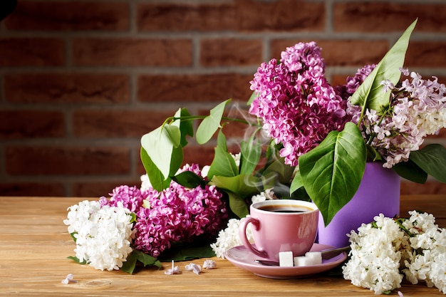 Nature morte avec des branches de lilas et une tasse de café sur une table en bois.