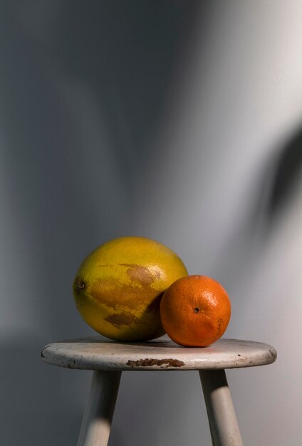 Photo nature morte de différents types d'agrumes sur un tabouret en bois blanc contre un mur blanc avec la lumière du soleil et l'ombre