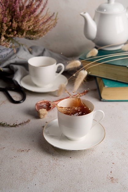 Photo nature morte avec du thé éclaboussant de tasse de thé, de livres et de fleurs