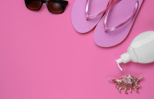 Nature morte d'été. Accessoires de plage. Tongs de plage rose à la mode, bouteille de crème solaire, lunettes de soleil, coquillage sur papier rose