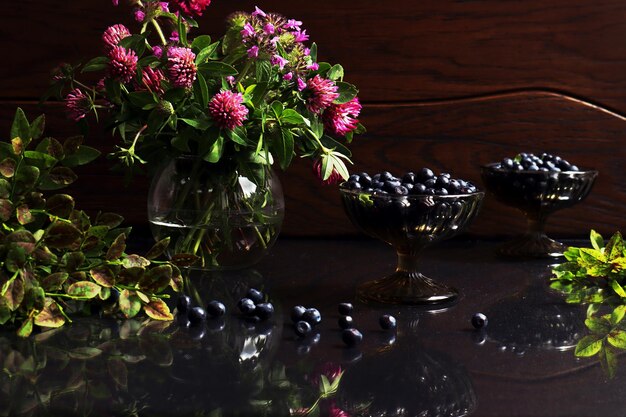 Nature morte d'été un bouquet de fleurs d'été dans un vase en verre bleuets dans des vases branches de bleuets sur une table en verre sur un fond en bois