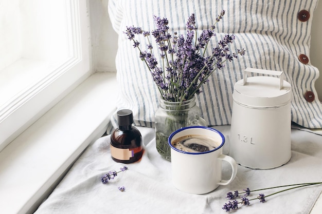 Nature morte d'été français Tasse de café lavande fleurs bouquet essence bouteille d'huile sur le rebord de la fenêtre Stock photo de style féminin composition florale avec des herbes Lavandula officinalis Scène rustique