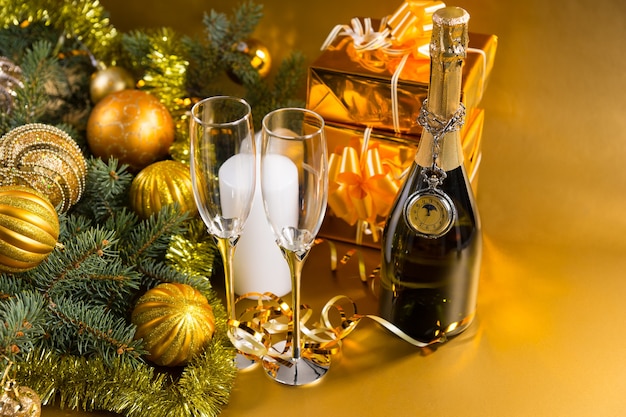 Nature morte festive - Montre de poche antique drapée sur une bouteille de champagne avec une paire de verres sur fond doré avec des cadeaux de Noël et des feuilles persistantes décorées de boules de Noël dorées et de guirlandes
