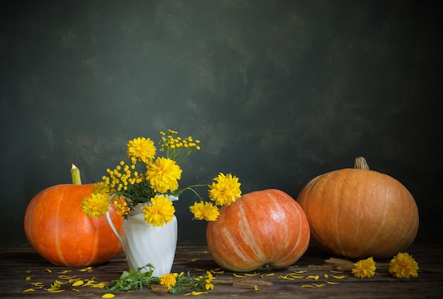 nature morte avec des fleurs jaunes et des citrouilles sur une vieille table en bois