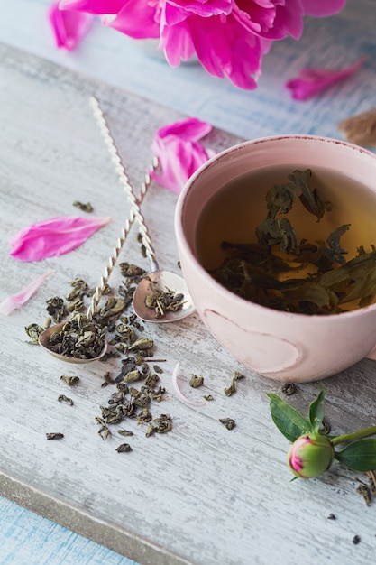 Nature morte avec des fleurs de pivoine rose et une tasse de thé à base de plantes ou vert sur fond de bois rustique