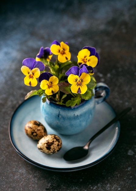 Nature morte avec des fleurs violettes et jaunes dans une cafetière bleue sur fond rustique