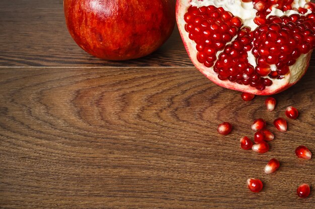 Nature morte - fruits de grenade entiers et coupés rouges et graines éparses sur une table en bois foncé