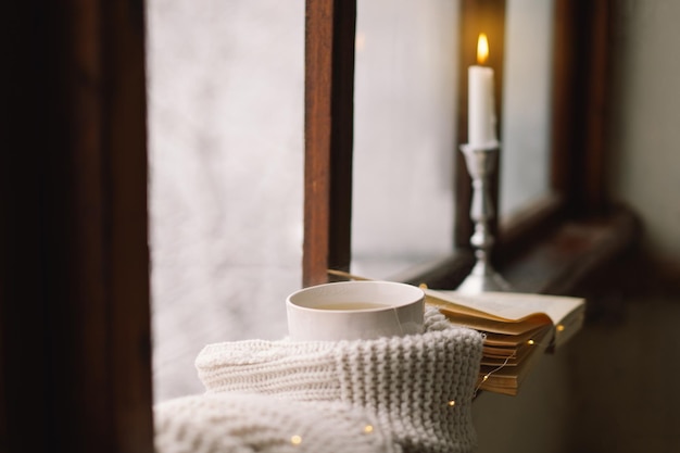 Nature morte d'hiver confortable Tasse de thé chaud et un livre ouvert avec un pull chaud sur un rebord de fenêtre en bois vintage Concept de maison confortable Maison douce