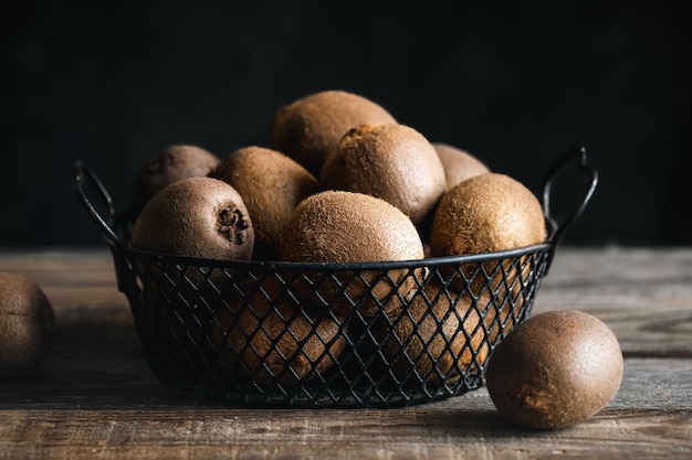 Nature morte avec des kiwis entiers dans un panier en métal gros plan sur un fond sombre