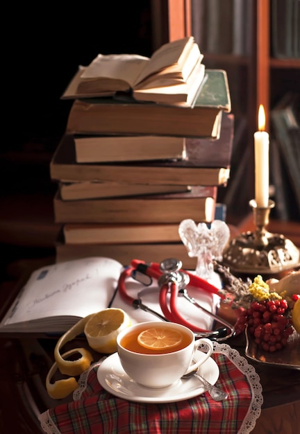 Nature morte médicale Une pile de livres vintage un phonendoscope une tasse de thé au citron un bloc-notes ouvert des plantes médicinales sur une table en bois