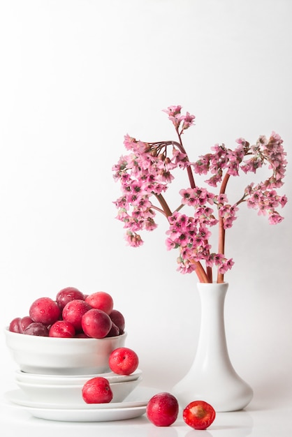 Nature morte minimale fraîche avec des fleurs de cerise prune et de violette rose sur la table dans des tons clairs blancs