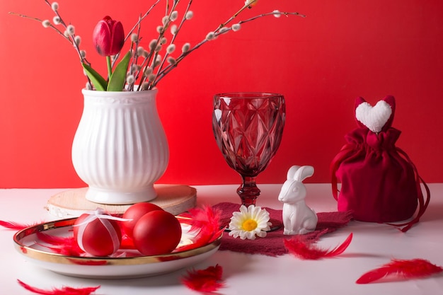 Nature morte de Pâques avec un lapin blanc sur fond rouge Un verre de vin et des œufs peints le concept de vacances de Pâques lumineuses