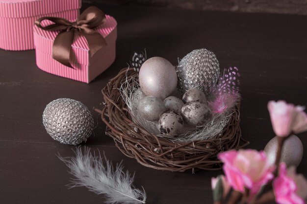 Nature morte de Pâques avec des oeufs de Pâques créatifs dans le nid et des plumes en discret