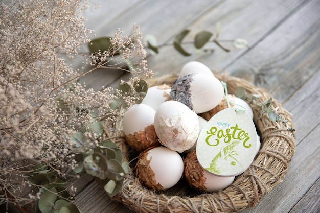 Nature morte de Pâques avec des oeufs de Pâques décorés et nid décoratif sur une surface en bois avec des brindilles sèches. Joyeuses Pâques souhaite le concept.