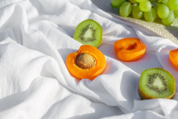 Nature morte et photo de nourriture. Le kiwi et l'abricot se trouvent sur un tissu froissé blanc sous les rayons du soleil contrastant