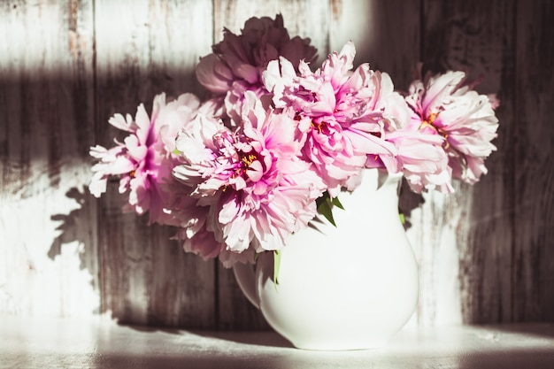 Nature morte avec des pivoines sur un mur en bois minable avec la lumière du soleil de la fenêtre