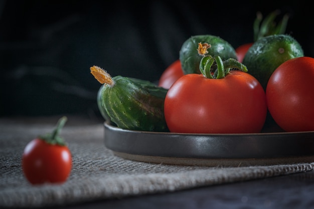 Nature morte rustique avec des légumes frais: tomates rouges, concombres verts, ail, aneth sur fond sombre.