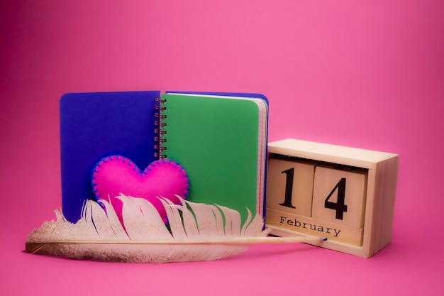 La nature morte de la Saint-Valentin avec du textile cousu à la main, un cœur rose, un cahier, une plume, un stylo et une date en bois.