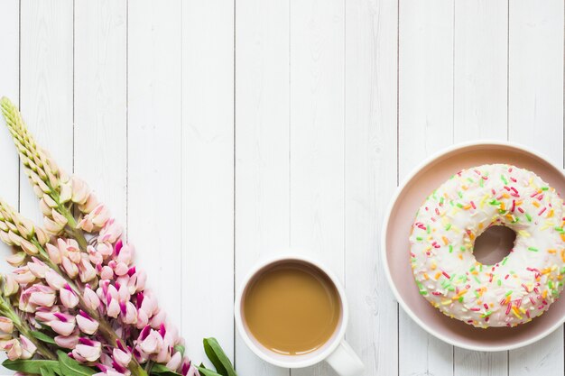 Nature morte avec une tasse de café et beignet de fleurs de lupin sur une table en bois clair. Espace de copie