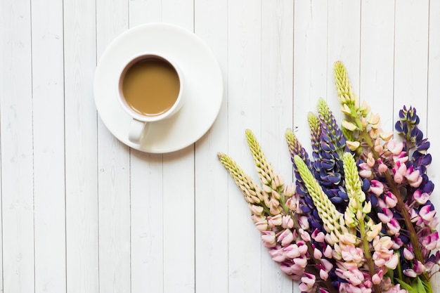 Nature morte avec une tasse de café et beignet de fleurs de lupin sur une table en bois clair.