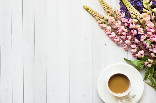 Nature morte avec une tasse de café et beignet de fleurs de lupin sur une table en bois clair.