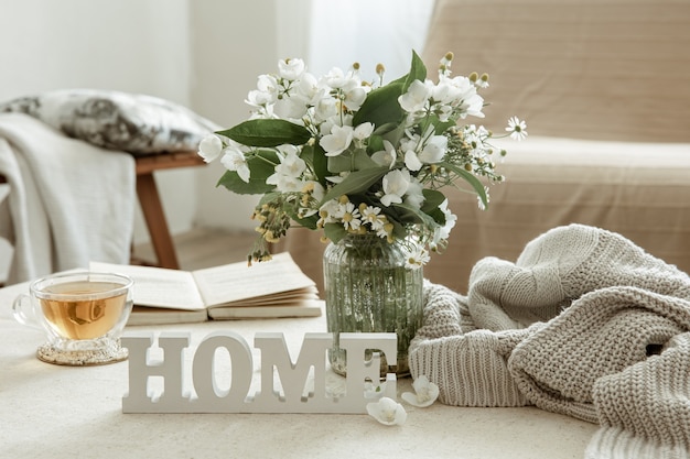 Photo nature morte avec une tasse de tisane, un bouquet de fleurs, un livre et un mot décoratif en bois à la maison.