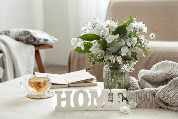 Nature morte avec une tasse de tisane, un bouquet de fleurs, un livre et un mot décoratif en bois à la maison.