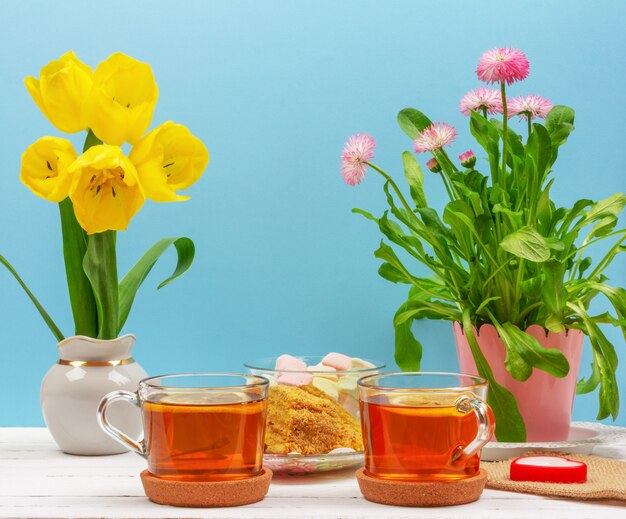 Nature morte avec des tasses de thé, des morceaux de gâteau, bouquet de fleurs roses, guimauve et tulipes jaunes