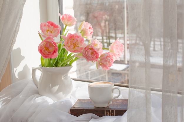 Nature morte un vase avec des tulipes et un vieux livre sur la fenêtre