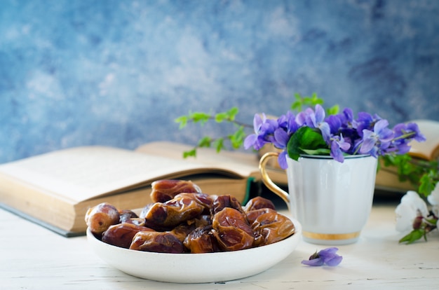 Nature morte avec violette dans une tasse blanche, vieux livres et fruits de la date dans une assiette. Floral romantique