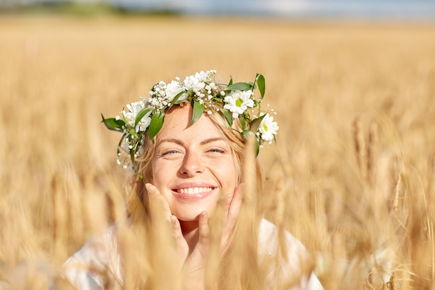 nature, vacances d'été, vacances et concept de personnes - visage d'une femme souriante heureuse ou d'une adolescente n dans une couronne de fleurs sur un champ de céréales