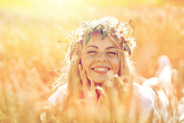 Photo nature, vacances d'été, vacances et concept de personnes - visage d'une femme souriante heureuse ou d'une adolescente n dans une couronne de fleurs sur un champ de céréales