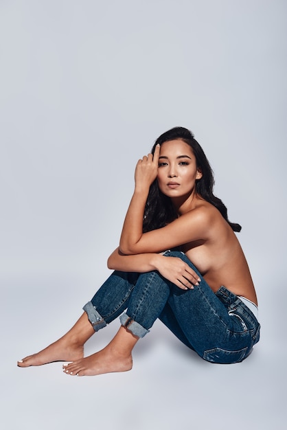 Naturel et beau. Jolie jeune femme regardant la caméra en position assise sur fond gris