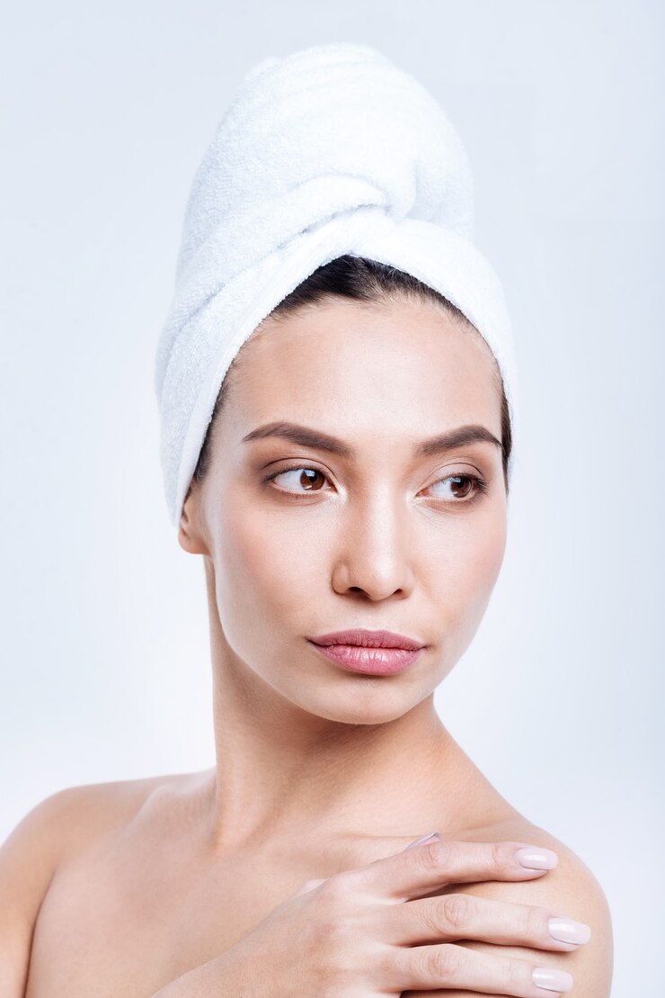 Photo naturellement belle. le portrait d'une charmante jeune femme aux épaules nues portant un turban serviette et touchant son épaule tout en posant contre un mur blanc
