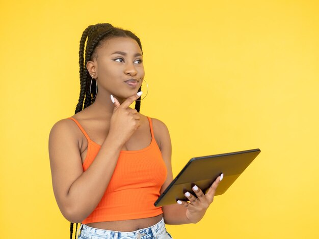 Navigation sur Internet Réseau numérique Technologie Gadget Pensée pensive Femme africaine à l'aide d'une tablette PC isolée sur fond jaune