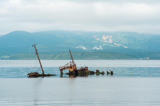 Navire coulé dans le contexte d'une baie de la mer avec des montagnes brumeuses en arrière-plan