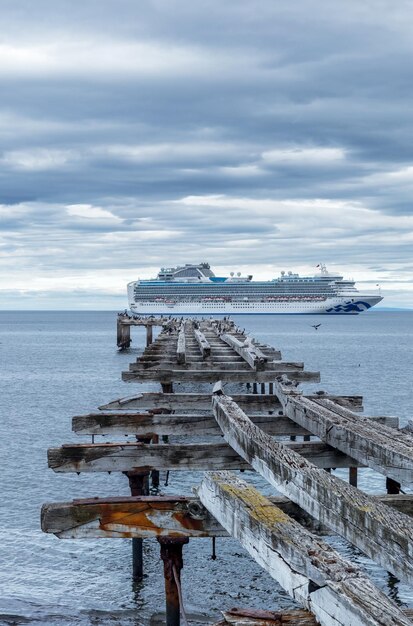 Photo un navire de croisière au-delà d'une jetée en bois détériorée dans un paysage marin bleu