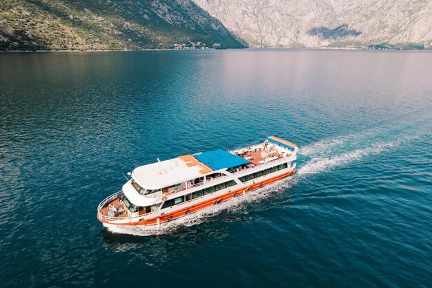 Un navire à deux étages coloré avec des touristes navigue sur la mer le long d'une crête de montagne