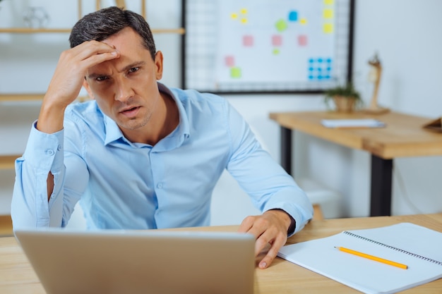 Ne m'irrite pas. Personne de sexe masculin attentif fronçant le front et assis sur son lieu de travail tout en ayant mal à la tête