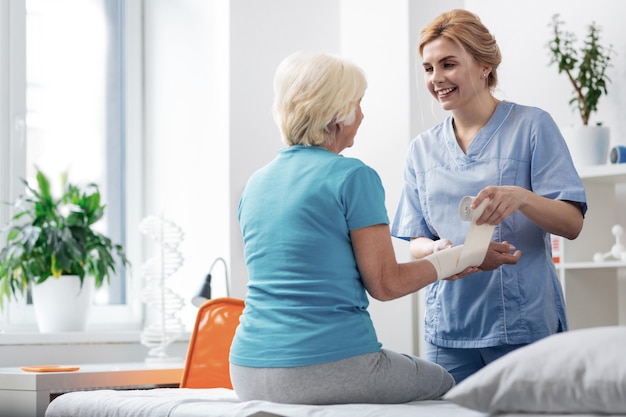 Ne t'en fais pas. Infirmière professionnelle gaie encourageant son patient tout en lui bandant la main