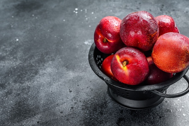 Nectarines biologiques rouges dans une passoire. Fond noir. Vue de dessus. Copiez l'espace.