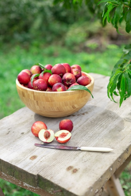 nectarines juteuses mûres dans un bol en bois sur une table en bois dans le jardin avec un couteau de style rustique