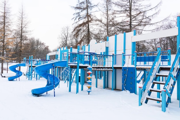 La neige bleue a couvert une grande aire de jeux vide avec des escaliers et des toboggans parmi les conifères