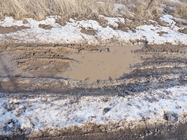 La neige fondante printanière, le chemin de terre, les flaques d'eau et la boue. Neige fondu.
