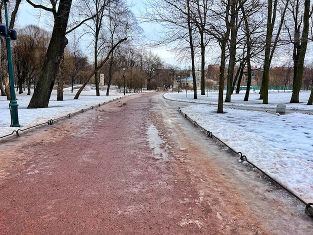 Neige fondante sale et gadoue sur la voie du parc sur les arbres nus du début du printemps se reflétant dans la flaque d'eau